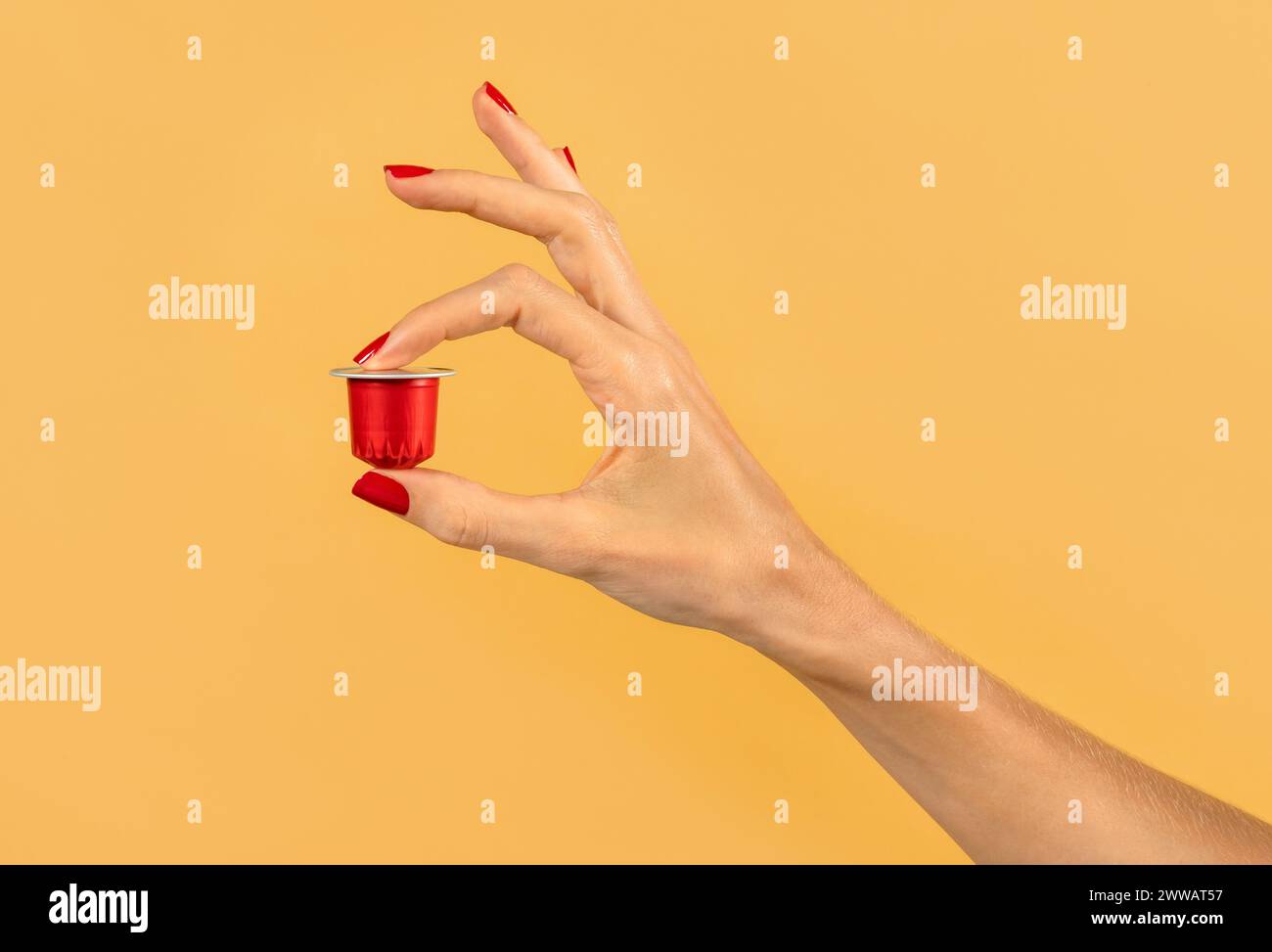 Nahaufnahme der Hand einer anonymen Frau, die rote Kaffeekapsel auf gelbem Hintergrund im Atelier hält Stockfoto
