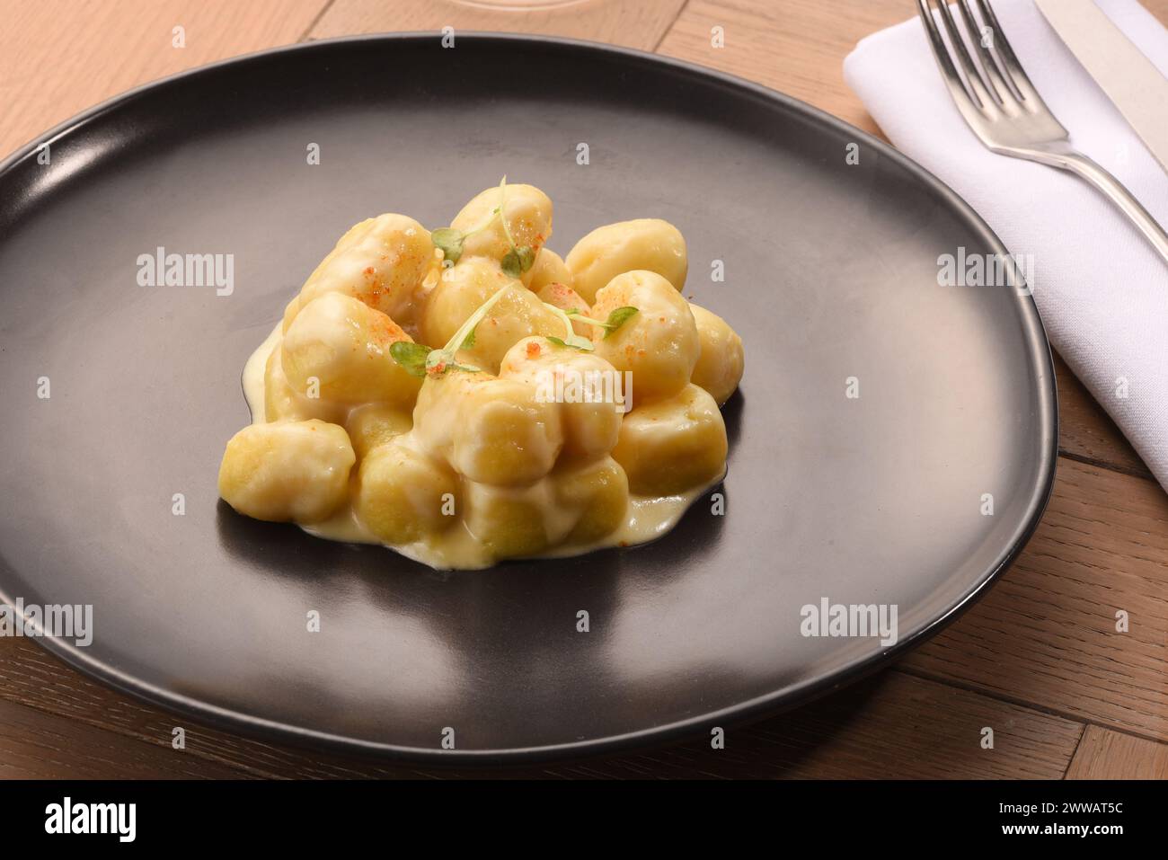 Köstliche italienische Gnocchi mit Weißkäsesauce serviert auf schwarzem Teller auf Holztisch im Restaurant Stockfoto