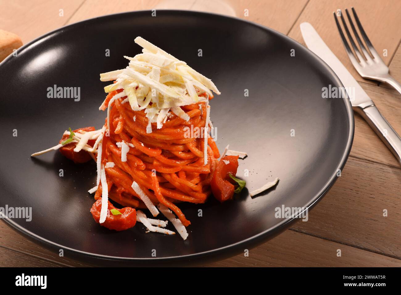 Appetitliche Spaghetti-Pasta mit Tomatensauce und Parmesan, serviert auf schwarzem Teller auf Holztisch im Restaurant Stockfoto