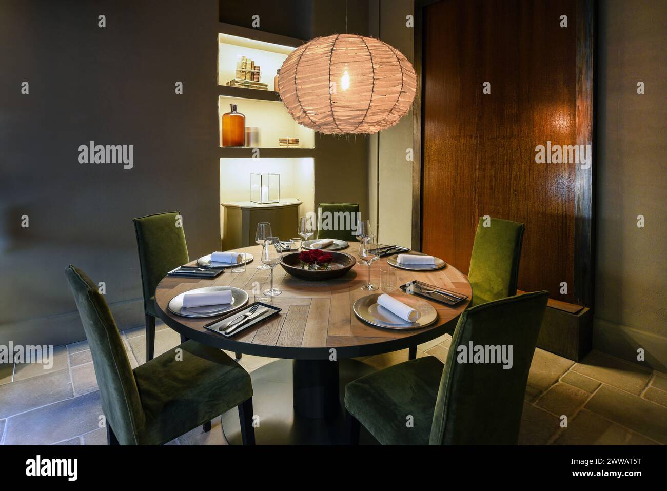 Beleuchtete Pendelleuchte über Stühlen um Holztisch mit Tellern und Weingläsern in der Restaurantecke Stockfoto