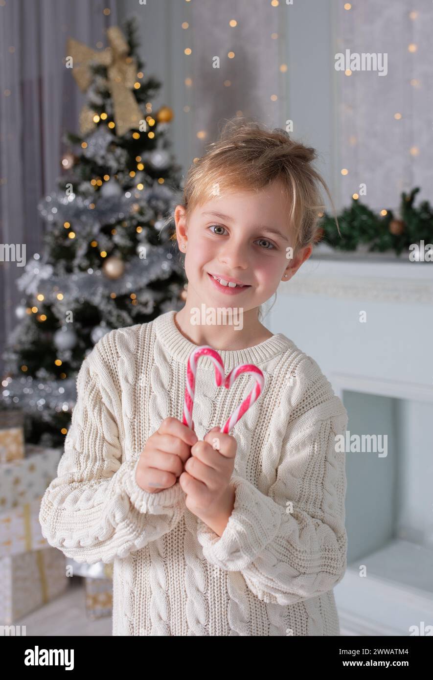 Weihnachtskerzenherz. Das kleine Neujahrsmädchen hat Weihnachtskaramell in Herzform zusammengestellt. Weihnachtsporträt in hellem Hintergrund Stockfoto