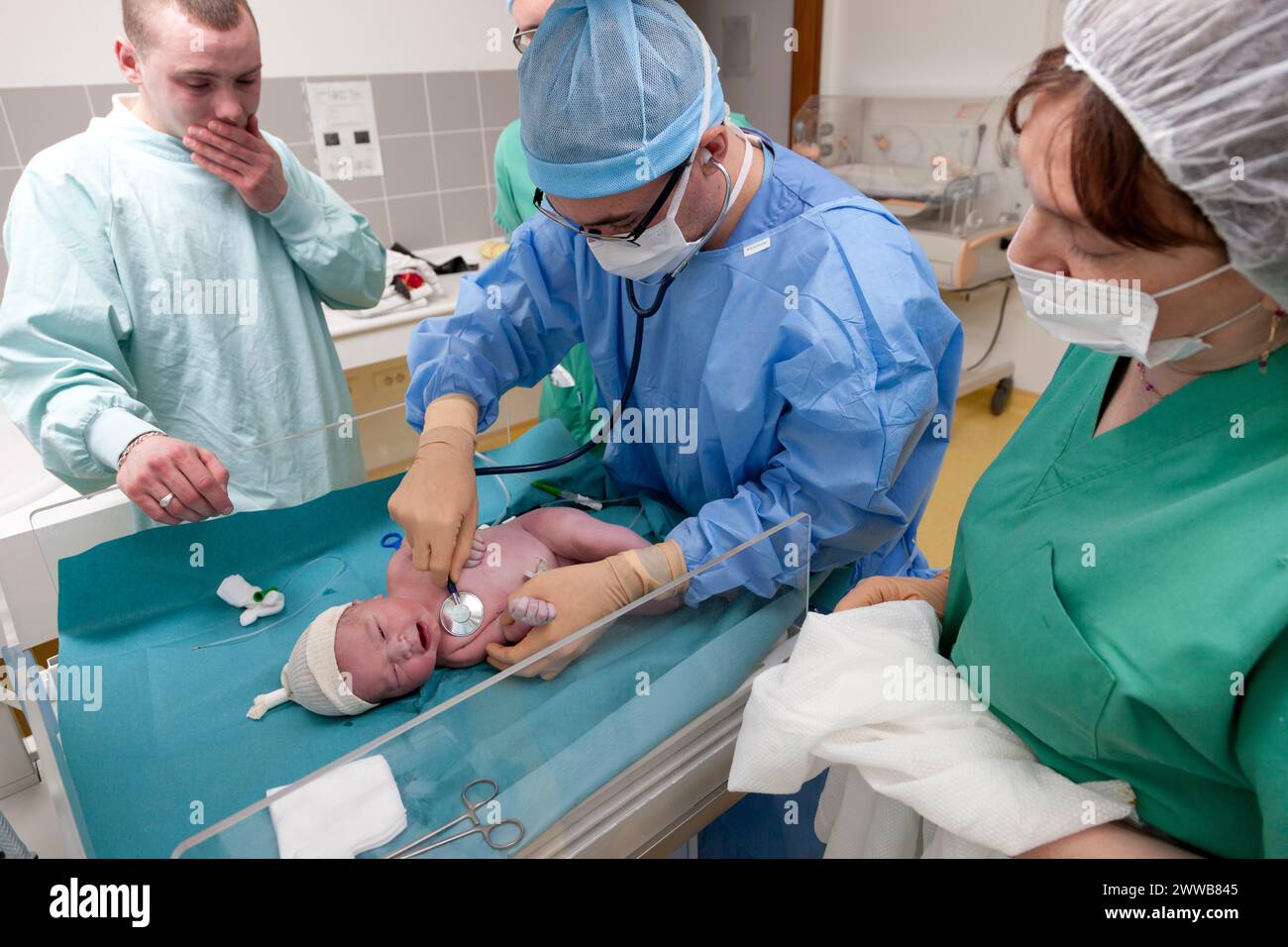 Unter dem bewegten Blick des Vaters führt ein Hebamme - Mann die ersten Untersuchungen durch, indem er die Herzfrequenz steuert. Stockfoto