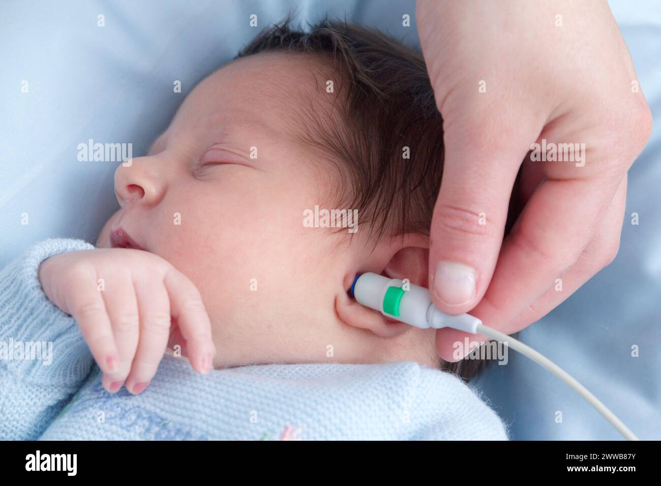 Krankenhaus. Mutterschaft. Hörtest - Eine Kinderbetreuerin führt einen Hörtest (OAE-Test - otoakustische Emissionen) an einem schlafenden Neugeborenen durch. Stockfoto