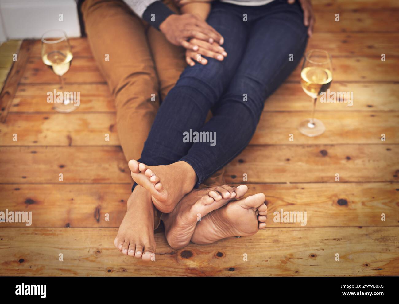 Wein, Füße und Paare entspannen zusammen auf Holzboden für ein romantisches Date in einem modernen Zuhause. Liebe, Champagner und Nahaufnahme von Mann und Frau Beinen mit Stockfoto