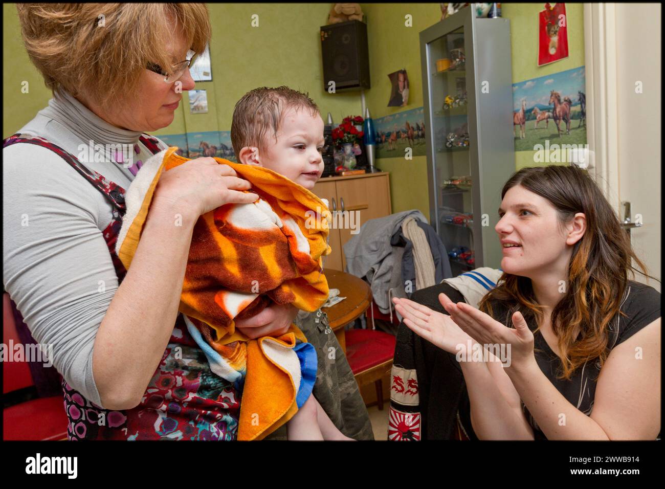 ASE - Kindersozialhilfe. Nach dem Bad bittet Isabelle ihre Mutter, ihn anzuziehen, während sie sich um Sarah kümmert. Stockfoto