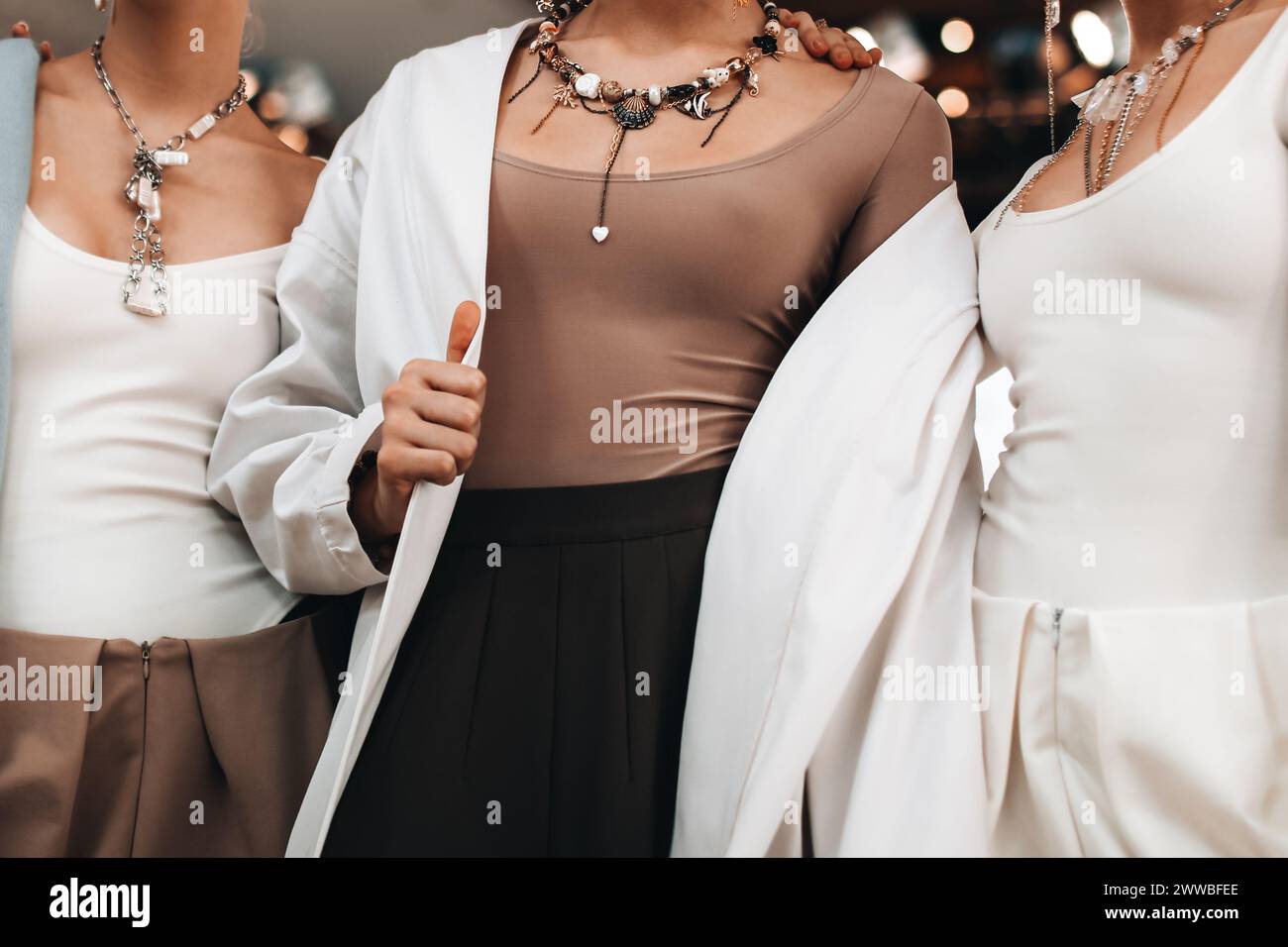 Schicke Accessoires, die an einem Damenhals hängen, modische Outfits, weiße Jacke und beiges Oberteil. Mode und Schmuck Stockfoto