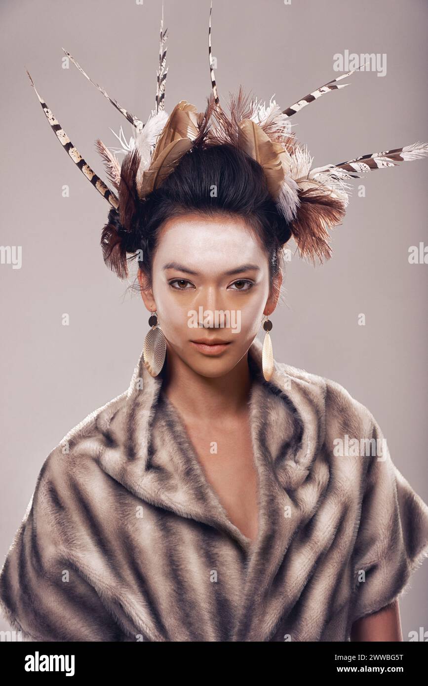 Frau, Porträt und Kunst mit Mode der Ureinwohner in traditioneller Kleidung auf grauem Atelierhintergrund. Weibliche Person mit Feder, Gesichtsfarbe oder Stockfoto