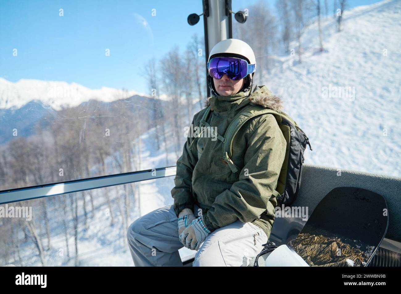 Beschaulicher Snowboarder in einer Gondelbahn mit Blick auf die verschneiten Pisten vor der Abfahrt. Stockfoto