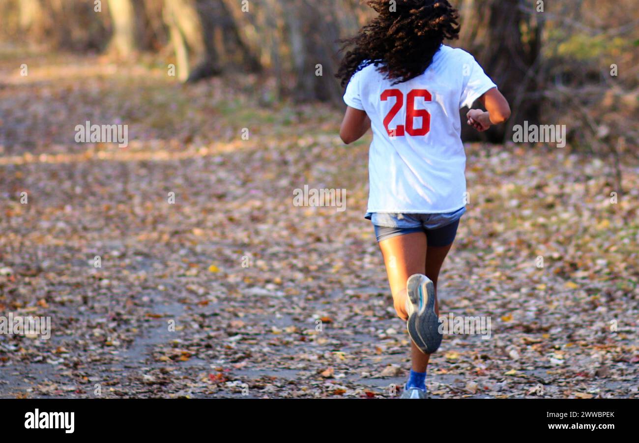 Rückansicht oder ein Mädchen, das auf einem Pfad voller bunter Blätter in einem Park läuft, im Herbsttraining für Langstreckenläufe. Stockfoto