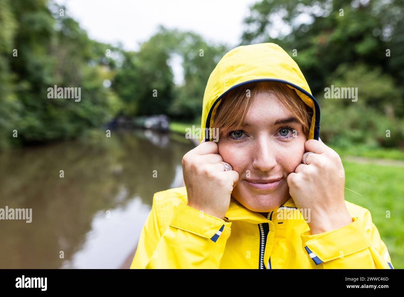 Lächelnde junge Frau mit gelbem Regenmantel im Wald Stockfoto