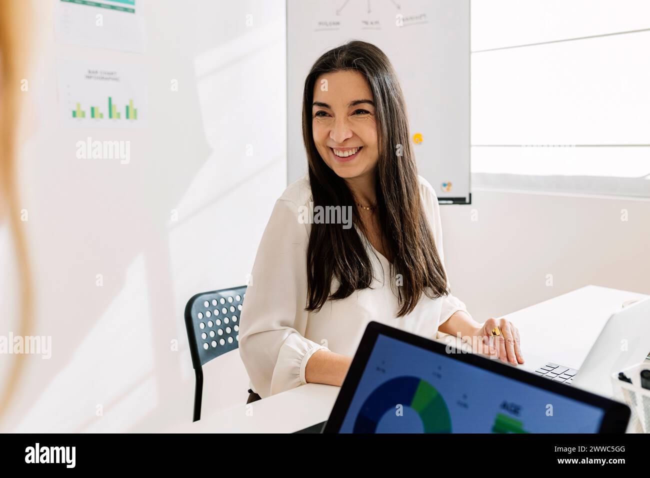 Lächelnde Geschäftsfrau, die mit einem Laptop am Schreibtisch sitzt Stockfoto