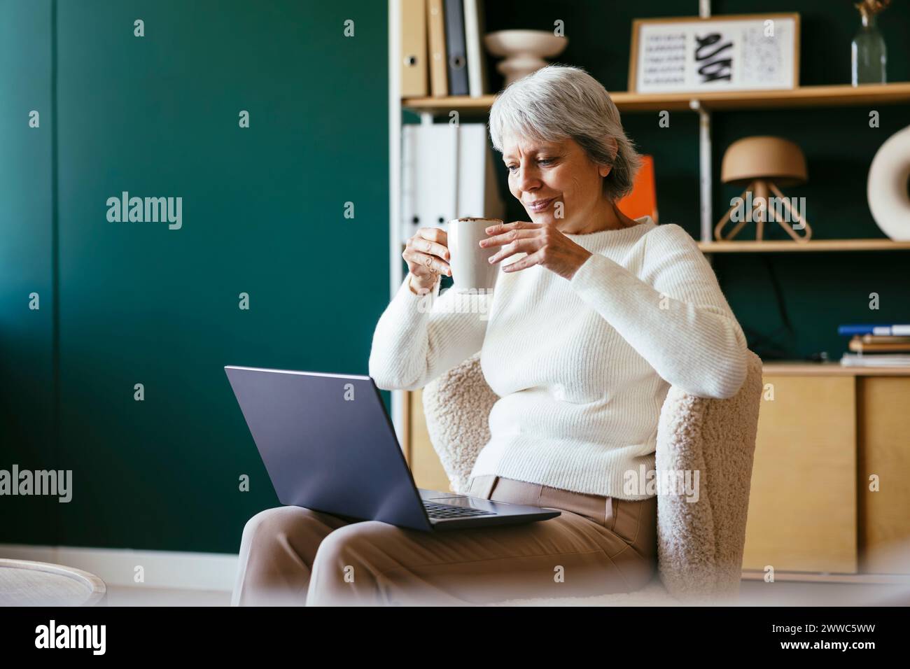 Reifer Freelancer, der Kaffee trinkt und im Home Office einen Laptop anschaut Stockfoto