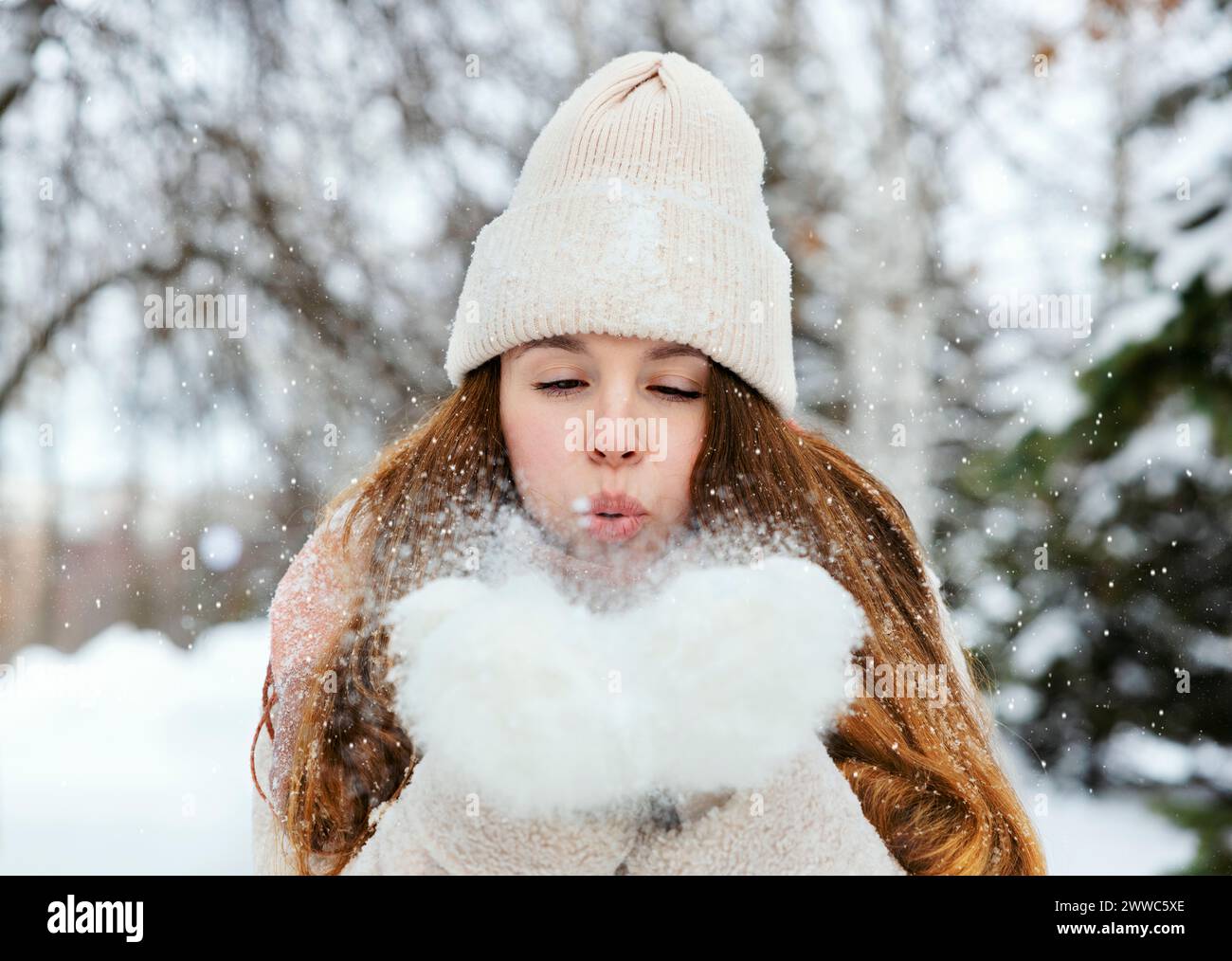 Verspielte Frau, die im Winterpark auf Schnee bläst Stockfoto