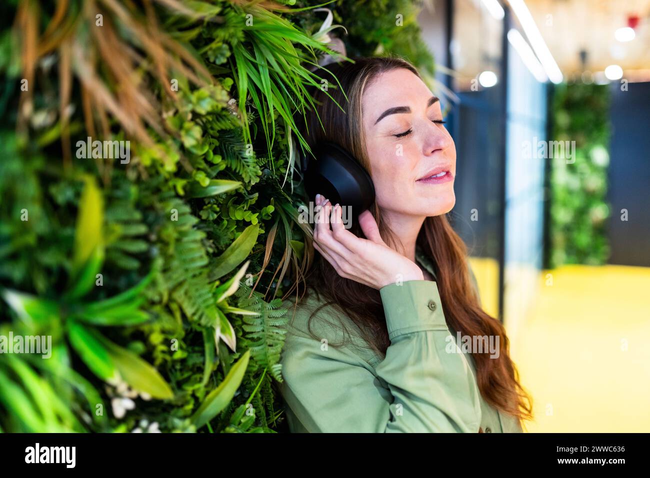 Lächelnde Geschäftsfrau, die im Büro über kabellose Kopfhörer Musik hört Stockfoto