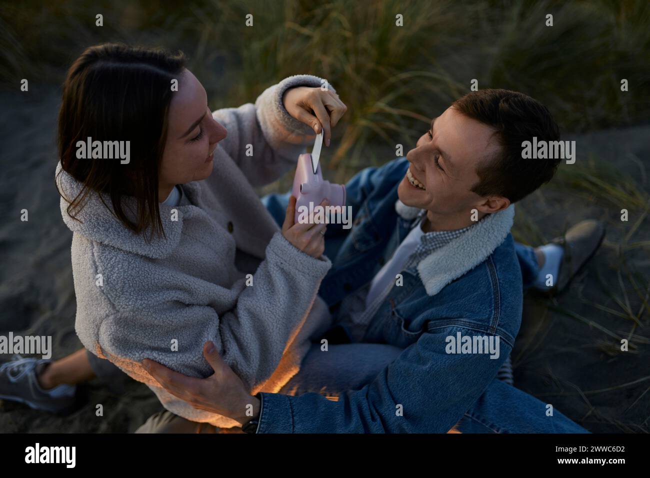 Glücklicher Mann, der die Freundin sieht, die am Strand einen Fotoabdruck von der Kamera herausnimmt Stockfoto