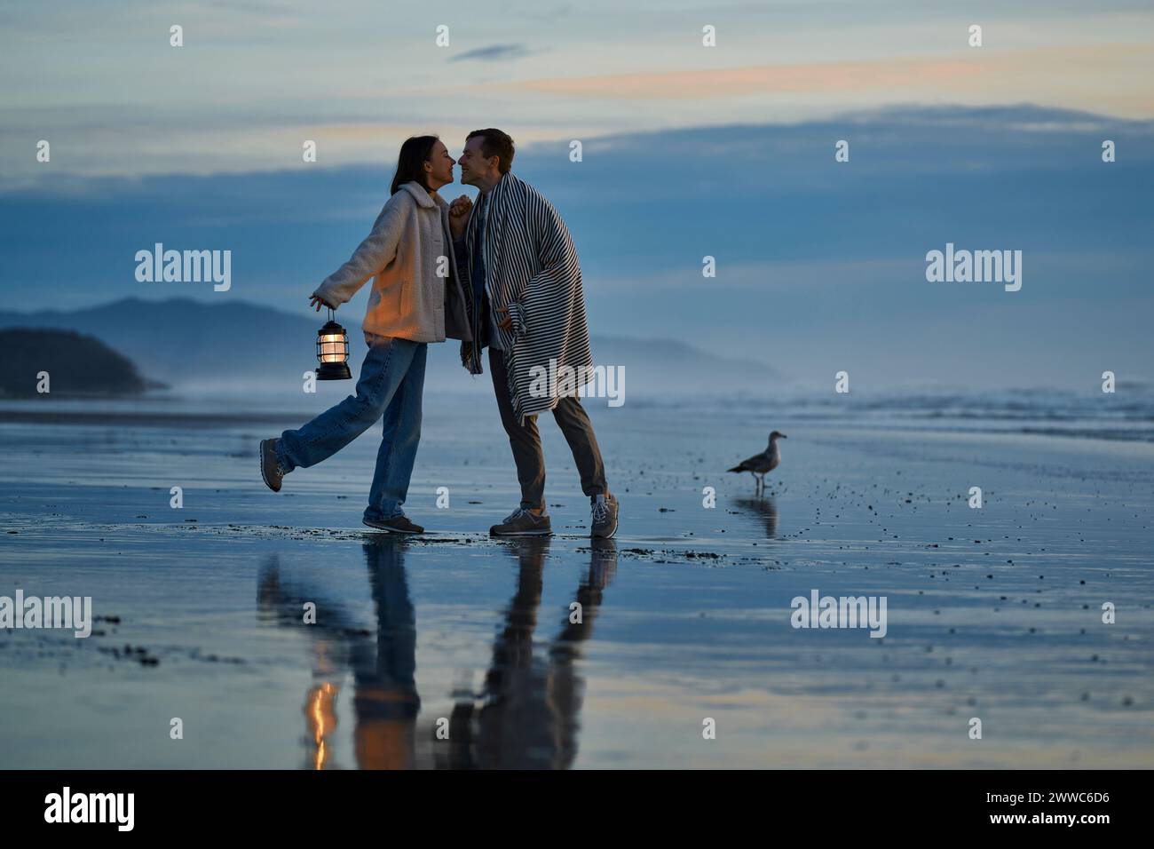 Ein junges Paar, das sich am Strand des Ozeans küssen will Stockfoto