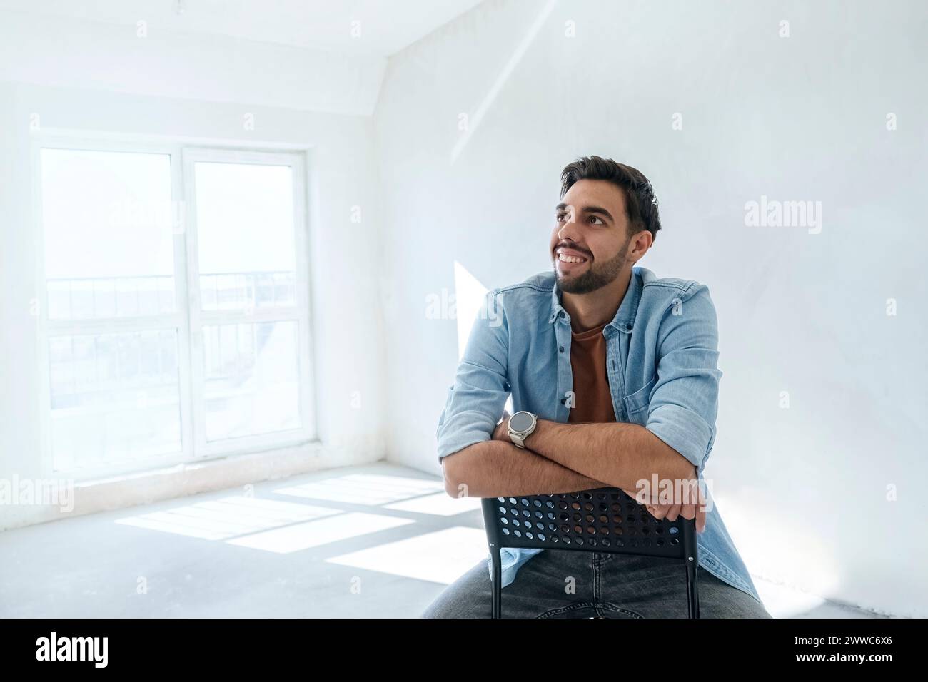 Ein nachdenklicher junger Mann sitzt auf einem Stuhl in einem neuen Zuhause Stockfoto