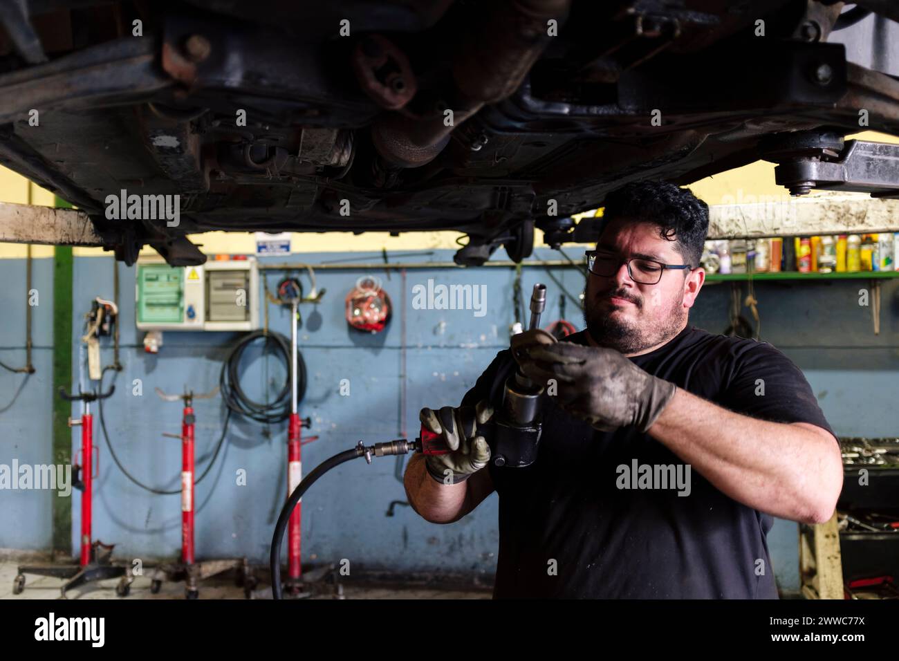 Mechaniker mit Schlagschrauber unter angehobenem Fahrzeug in der Werkstatt Stockfoto