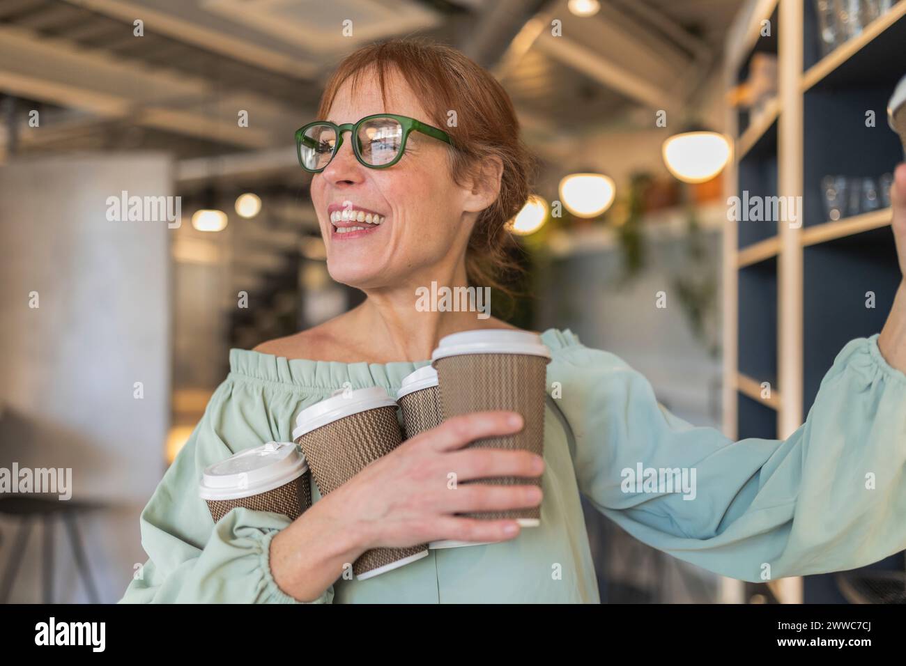 Glückliche Geschäftsfrau, die Einwegkaffeetassen im Bürocafé hält Stockfoto