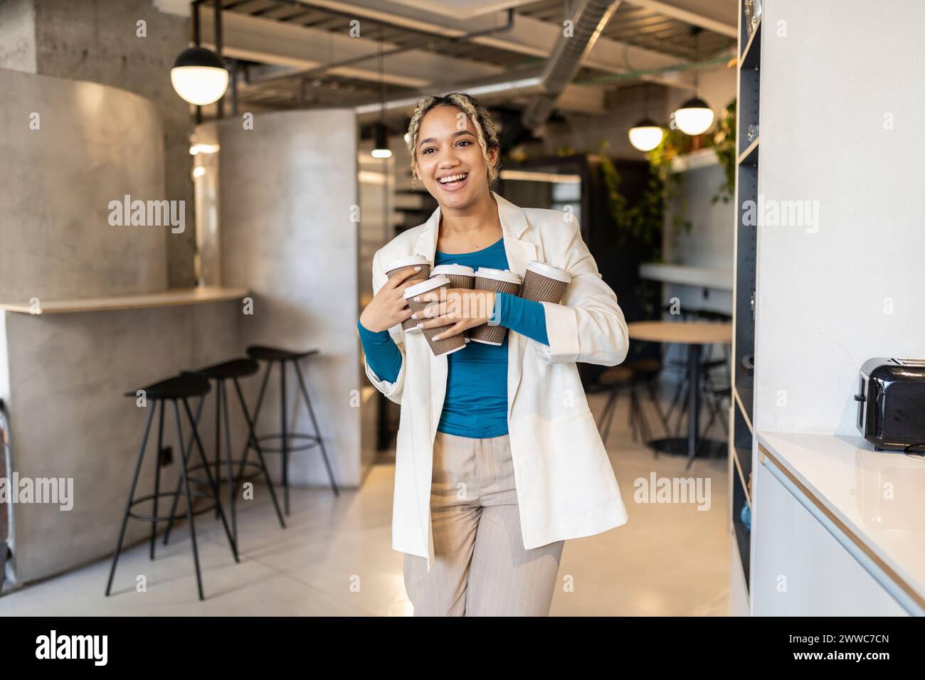 Junge Geschäftsfrau, die Kaffee in Einwegbechern im Bürocafé trägt Stockfoto