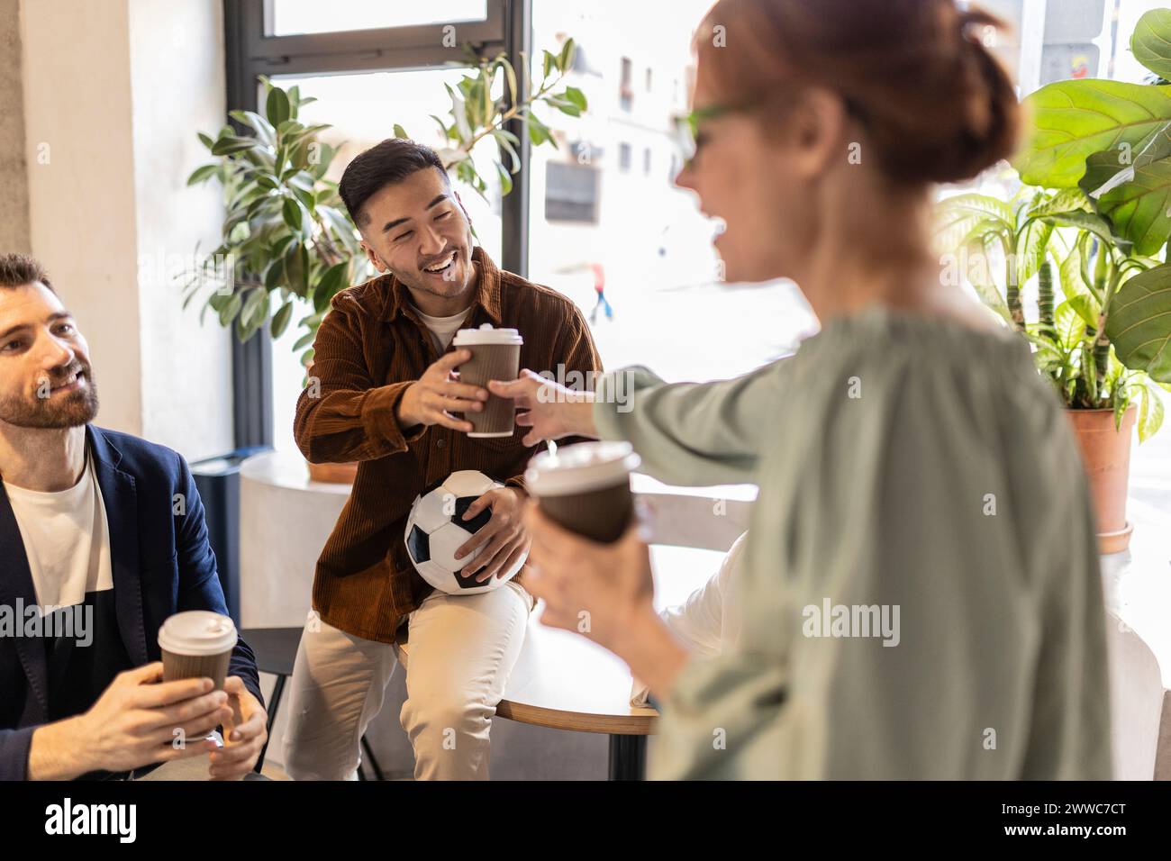 Lächelnder Geschäftsmann, der Einwegkaffee von einem Kollegen im Bürocafé nimmt Stockfoto