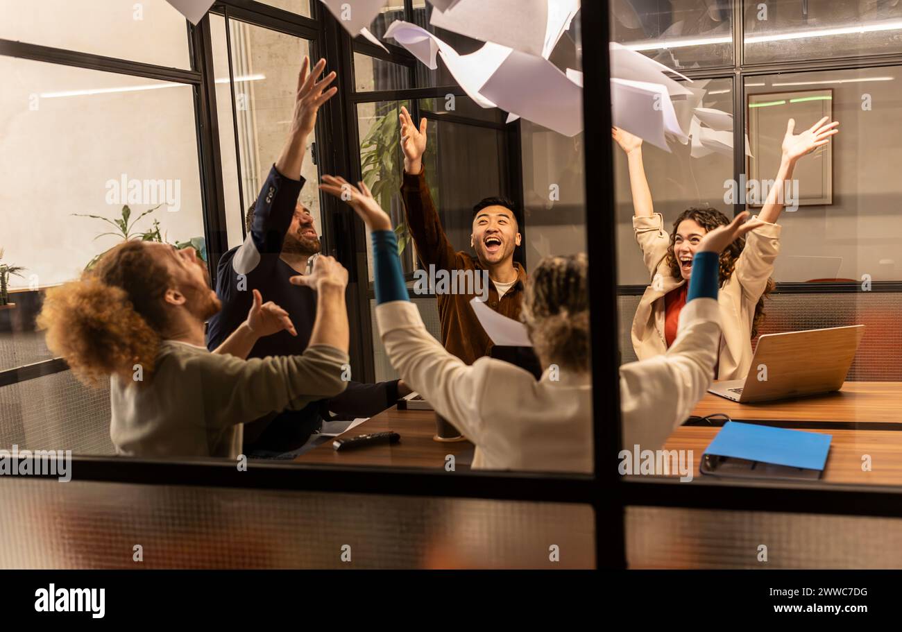 Fröhliche Geschäftskollegen werfen Papiere durch ein Glasfenster im Büro Stockfoto