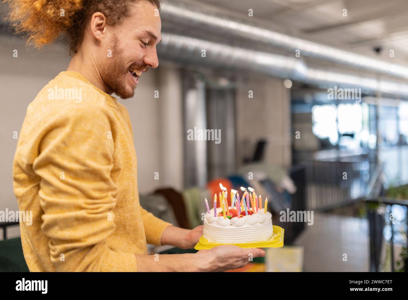 Glücklicher Geschäftsmann, der im Büro eine beleuchtete Geburtstagskuche hält Stockfoto
