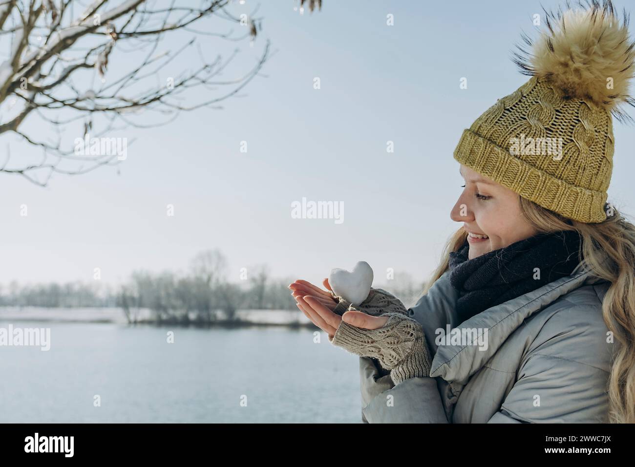 Glückliche Frau mit herzförmigem Schneeball in der Nähe des Sees Stockfoto