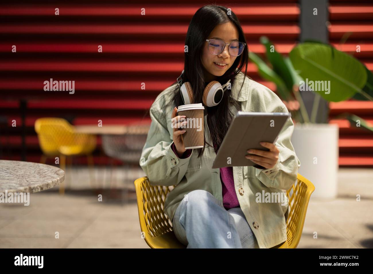 Lächelnde junge Frau, die eine Kaffeetasse hält und einen Tablet-PC im Straßencafé benutzt Stockfoto