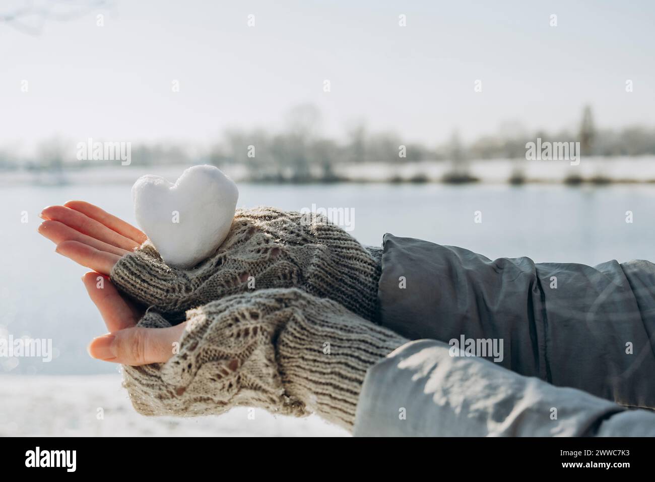 Hände einer Frau, die einen herzförmigen Schneeball in der Nähe des Sees hält Stockfoto