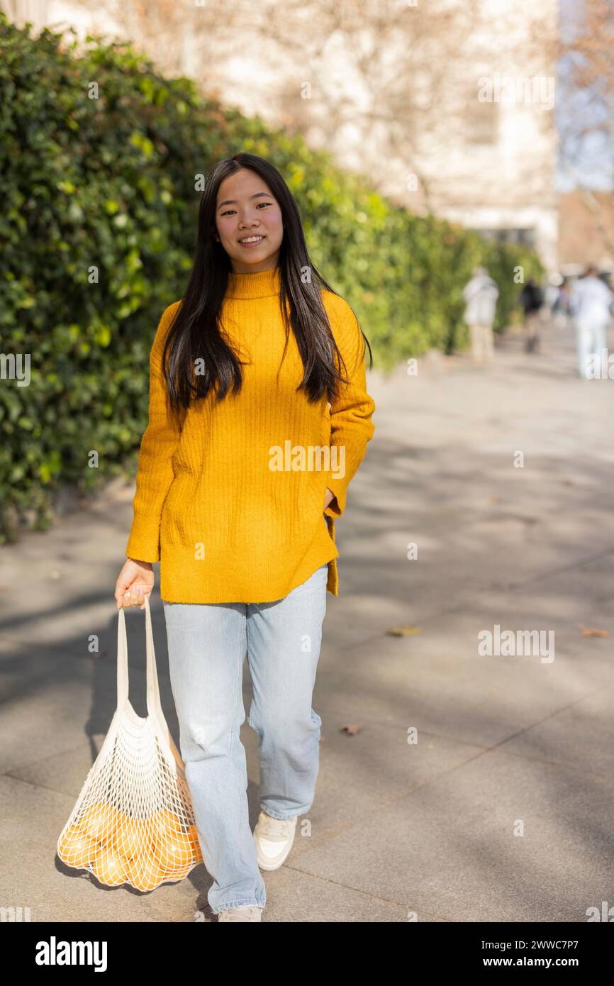 Lächelnde Frau, die mit einer Tüte Orangen auf dem Fußweg läuft Stockfoto