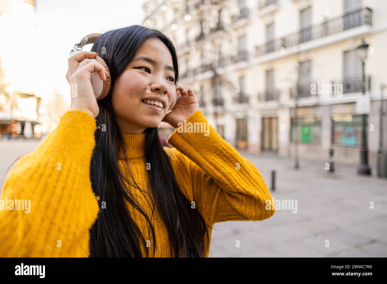 Glückliche junge Frau, die in der Nähe des Gebäudes kabellose Kopfhörer trägt Stockfoto