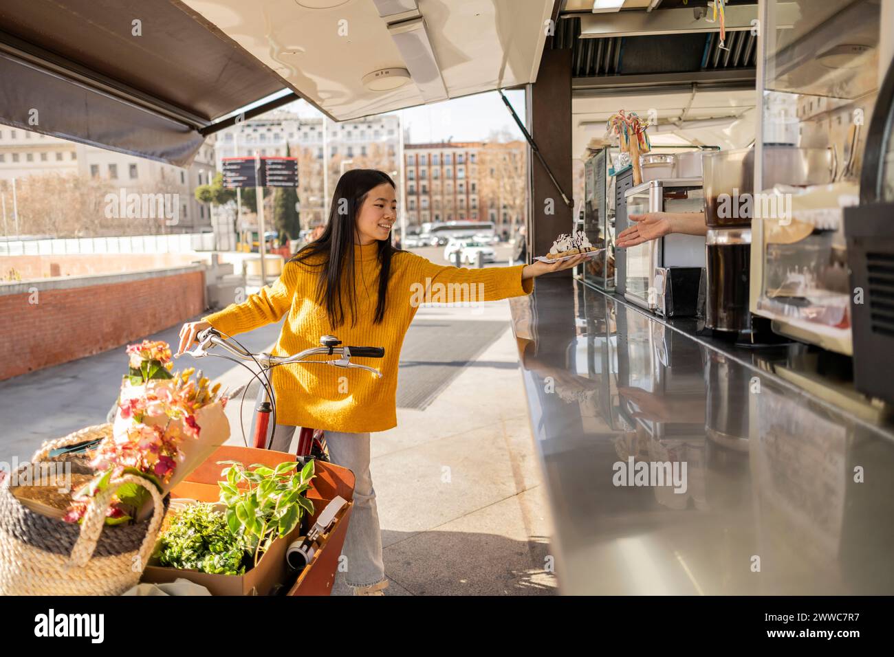 Glückliche junge Frau, die mit Lastenfahrrad steht und Dessert im Laden kauft Stockfoto