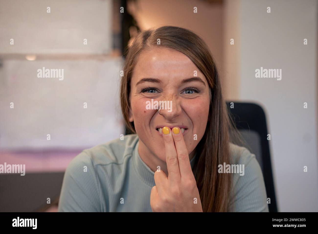 Verspielte Frau, die im Büro mit Fingern auf den Zähnen neckt Stockfoto