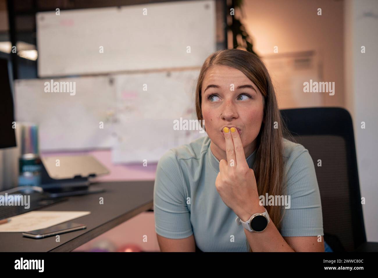 Junge Geschäftsfrau, die im Büro mit Fingern auf den Lippen sitzt Stockfoto
