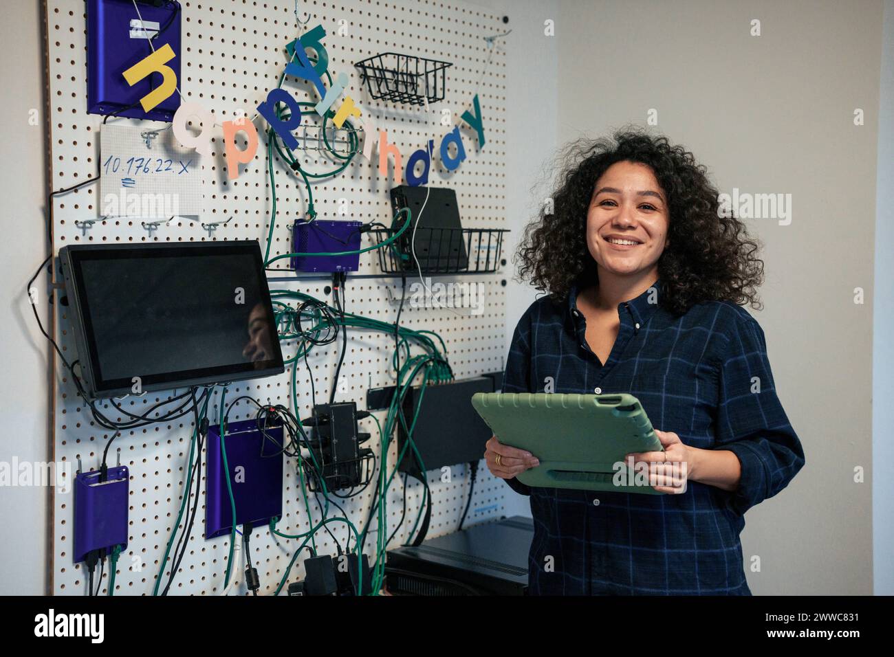 Lächelnder Ingenieur, der den Tablet-PC hält und in der Nähe von Netzwerkkabeln auf der Platine steht Stockfoto