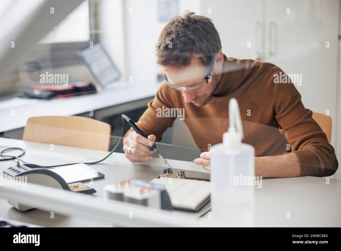Fokussierter Ingenieur, der Maschinenteile durch Lötkolben in der Werkstatt repariert Stockfoto