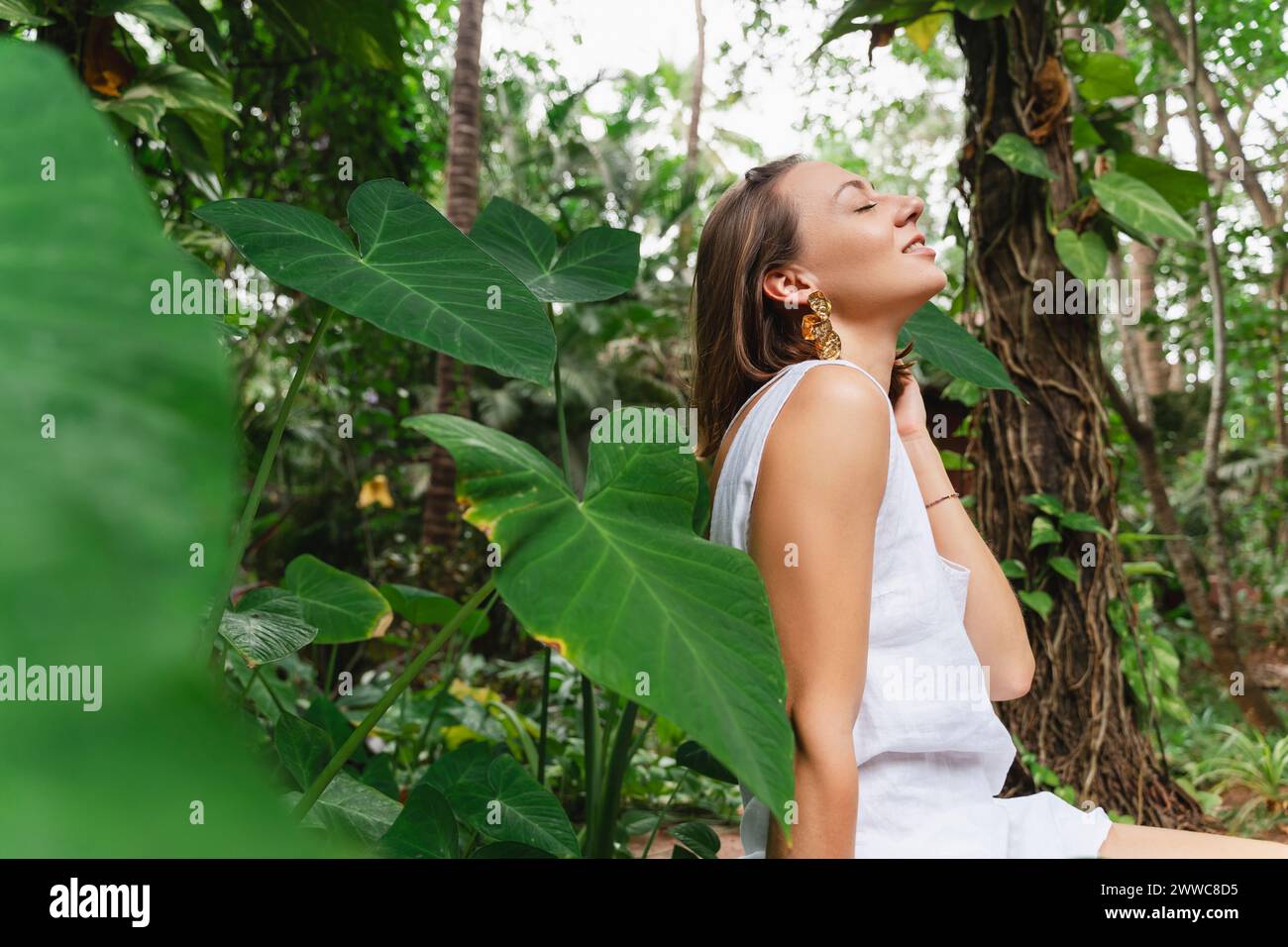 Lächelnde Frau, die im tropischen Garten sitzt Stockfoto