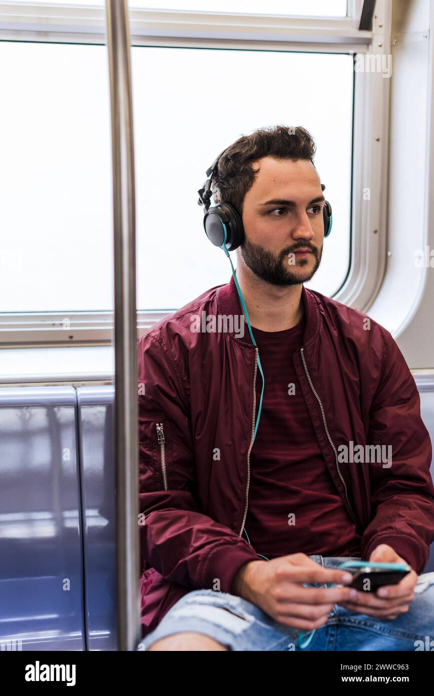 Junger Mann, der im Zug Musik über Kopfhörer hört Stockfoto
