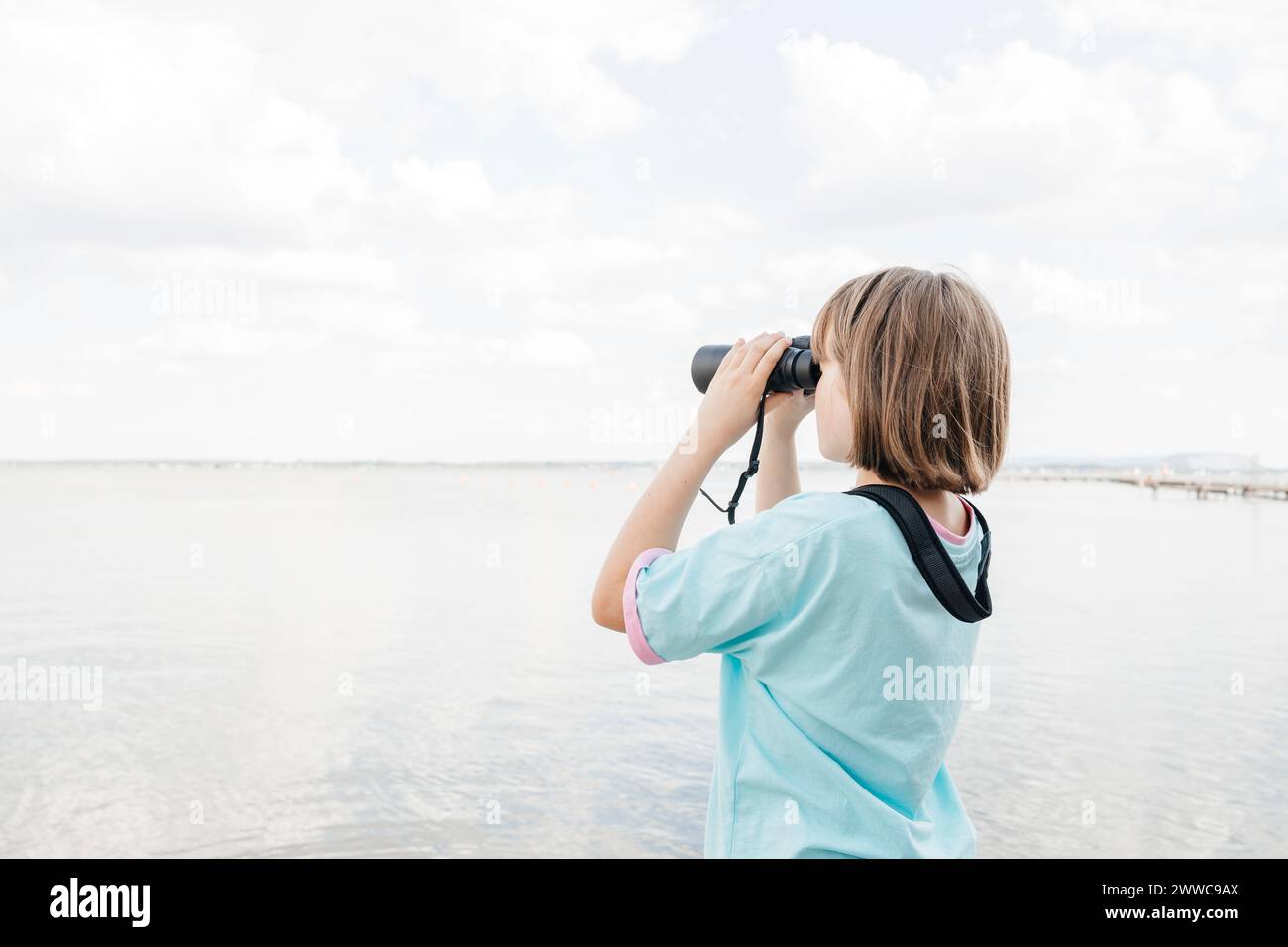 Mädchen, das durch ein Fernglas auf den See schaut Stockfoto