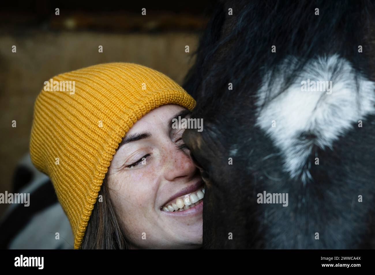 Glückliche Frau mit geschlossenen Augen in der Nähe eines Piebaldpferdes im Stall Stockfoto