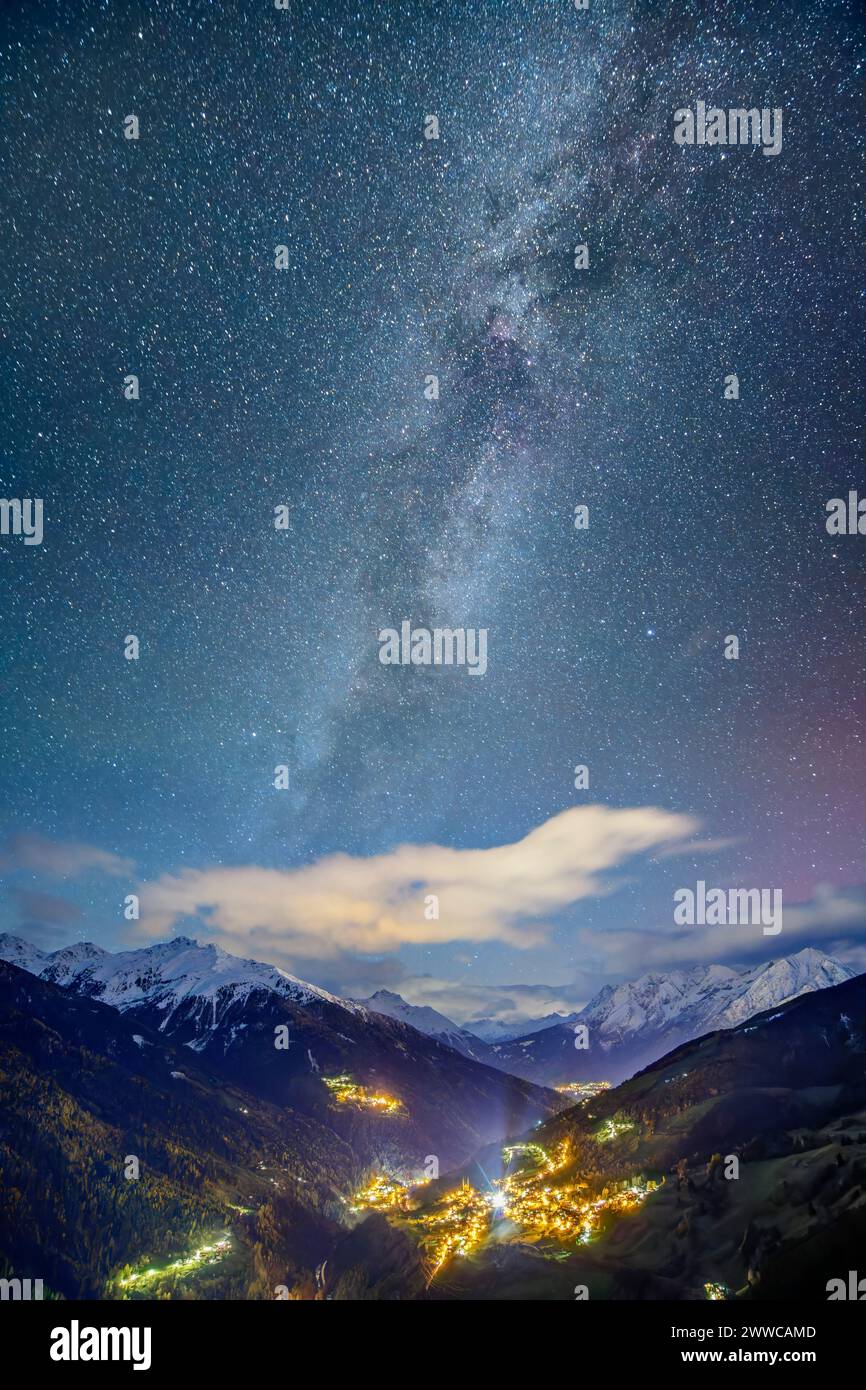 Österreich, tirol, Fliess, Milchstraßengalaxie gegen Sternenhimmel über der beleuchteten Stadt in den Lechtaler Alpen Stockfoto