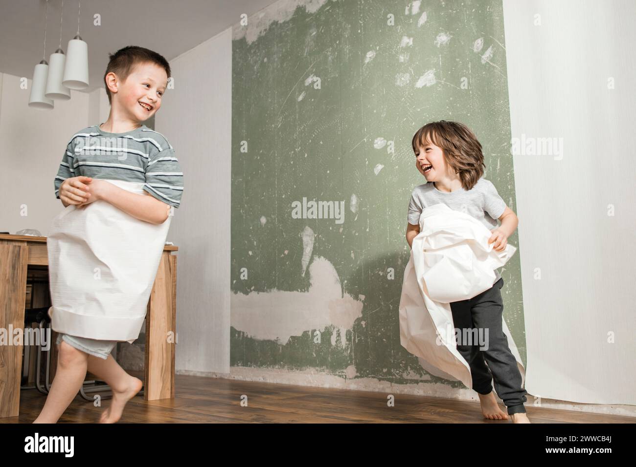 Verspielte Brüder, die in Tapeten gehüllt sind, laufen zu Hause Stockfoto