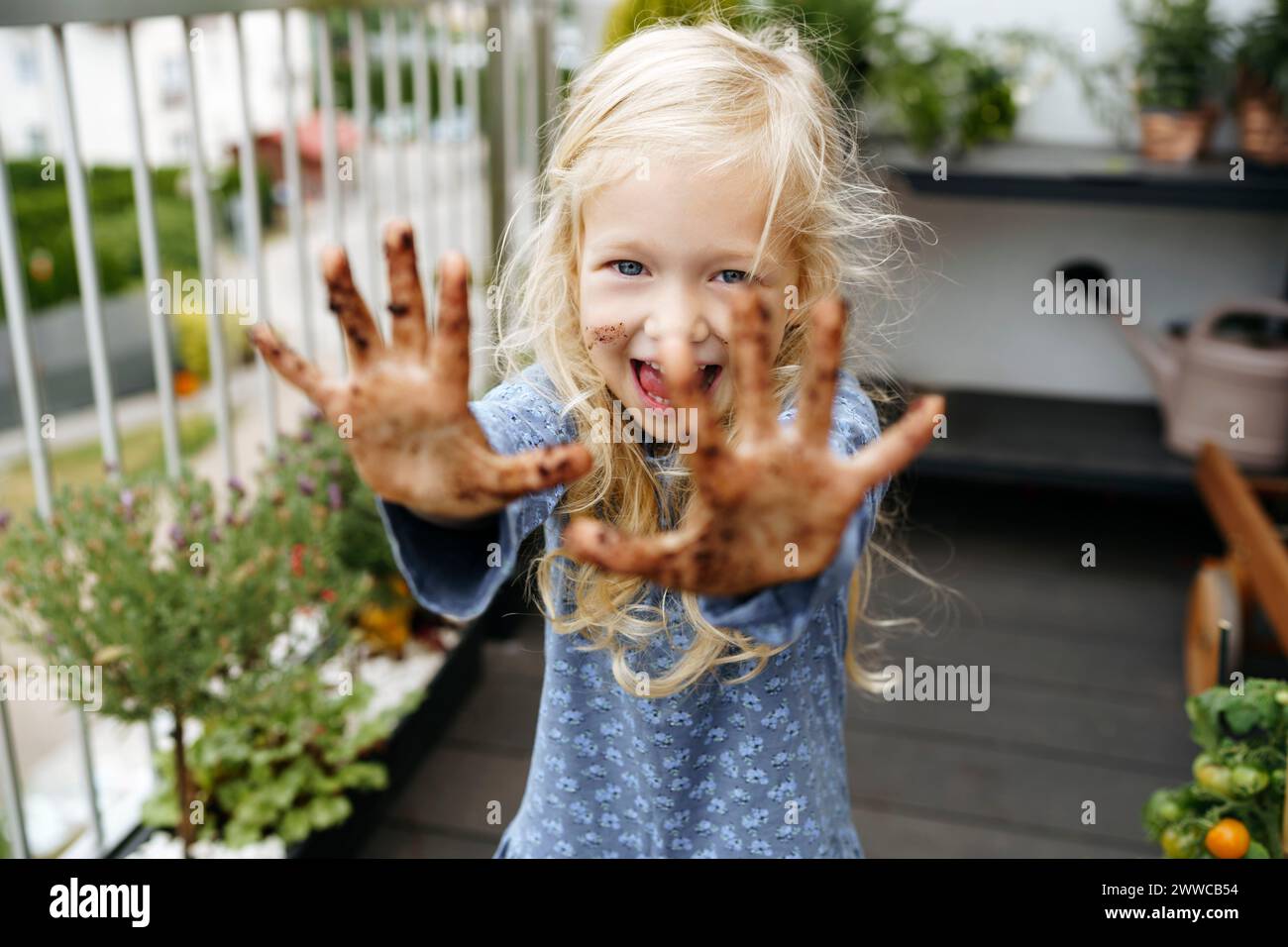 Fröhliches Mädchen, das im Balkongarten Hände voller Dreck zeigt Stockfoto