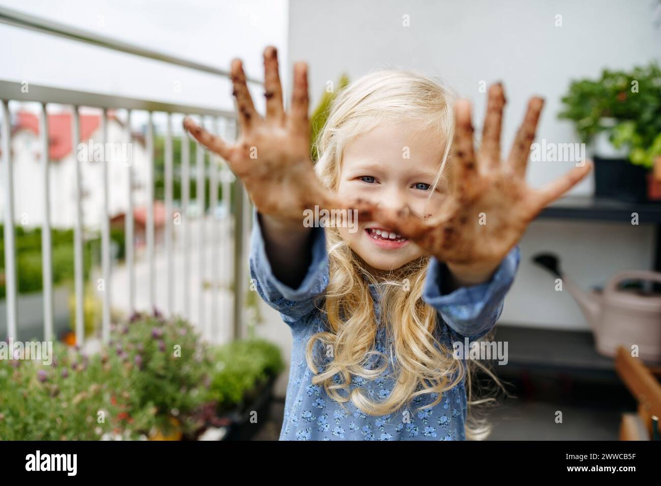 Lächelndes Mädchen, das Hände auf dem Balkon mit Dreck bedeckt zeigt Stockfoto