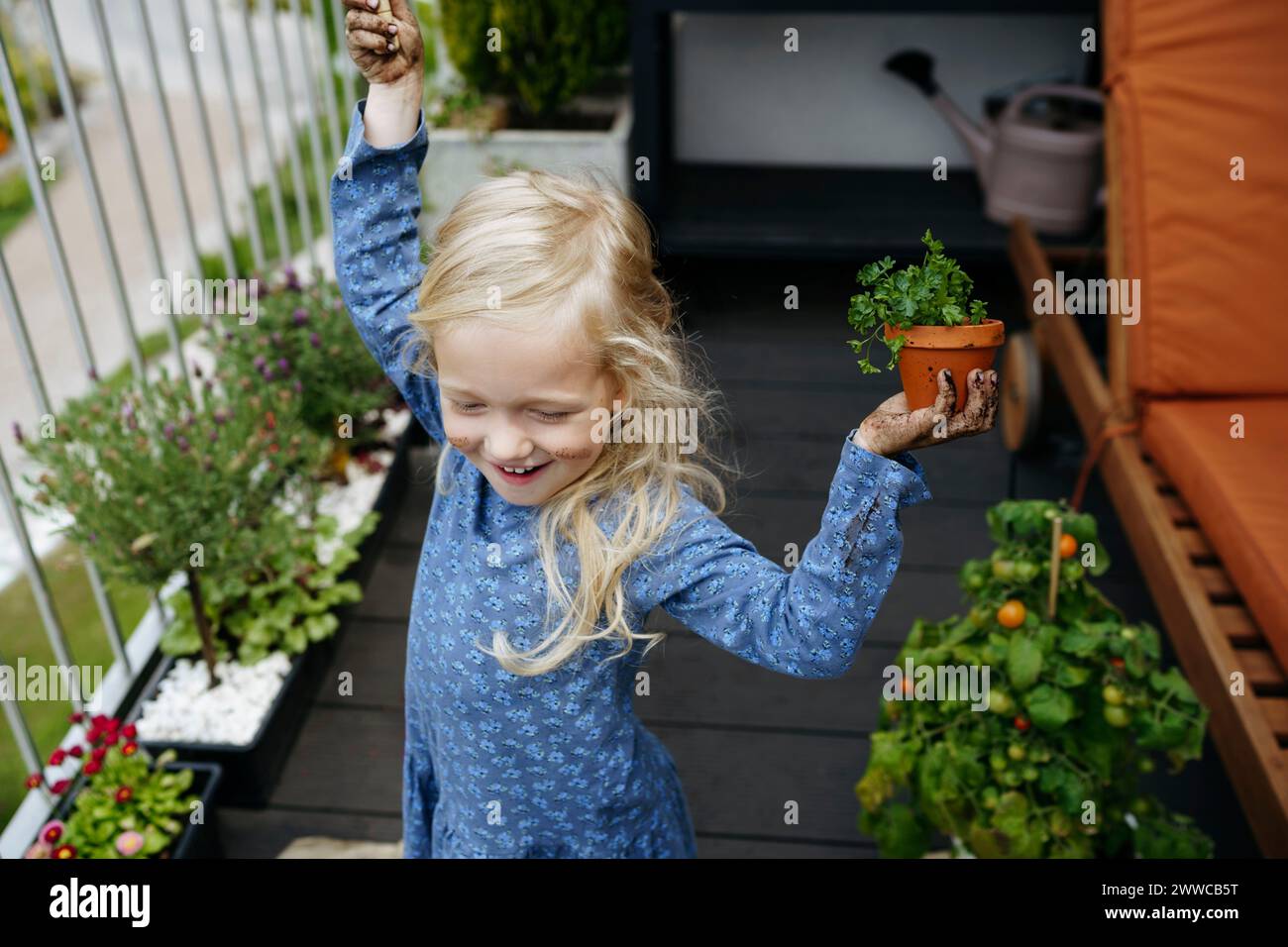 Fröhliches Mädchen, das Pflanzen im Balkongarten hält Stockfoto