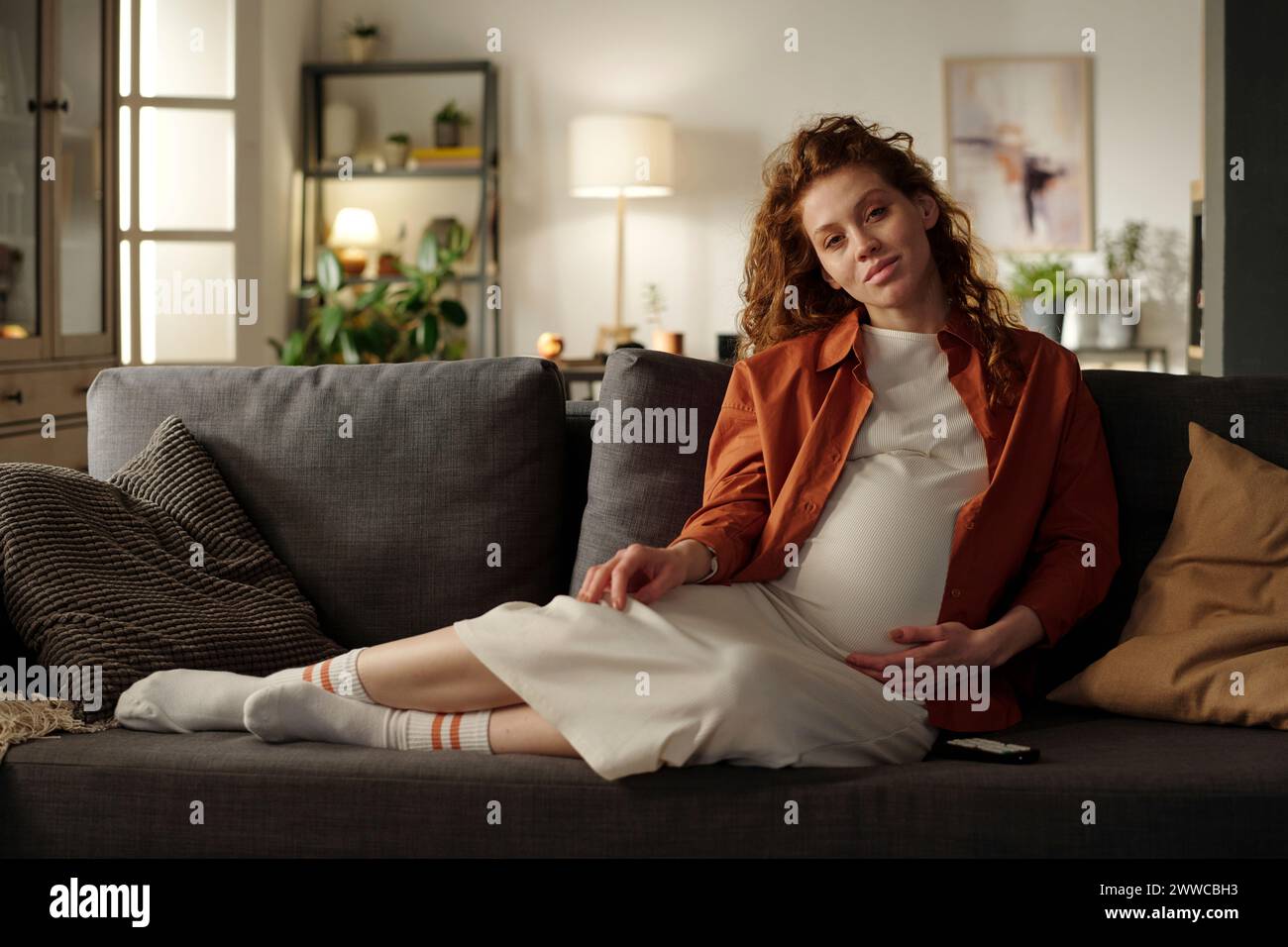 Junge werdende Frau, die im Wohnzimmer auf Sofa sitzt Stockfoto