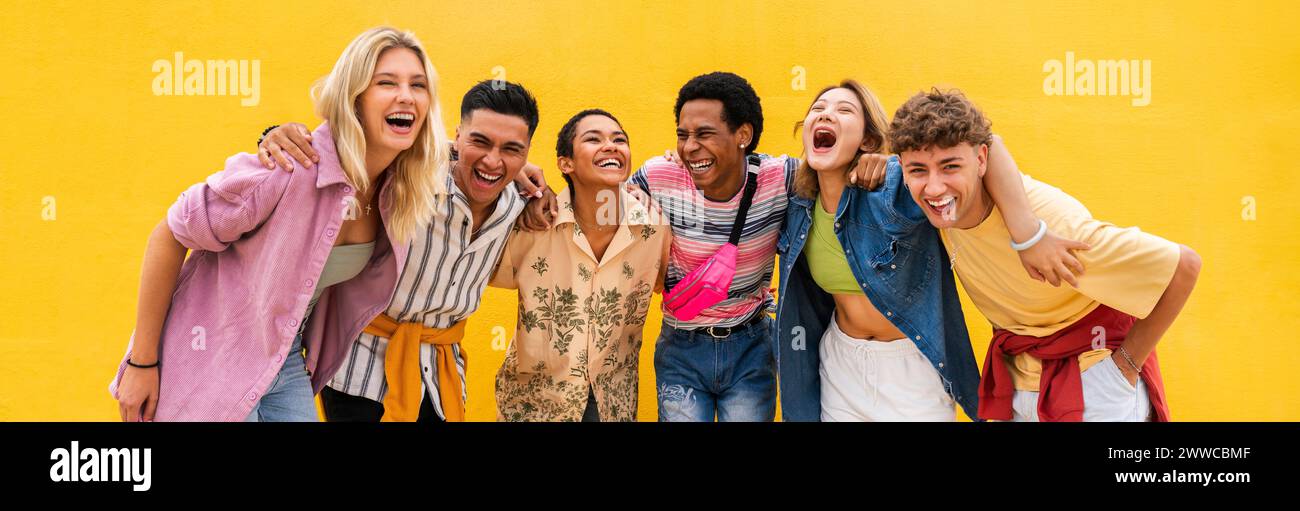 Sorglose Freunde in bunten Kleidern, die mit Armen vor der gelben Wand stehen Stockfoto