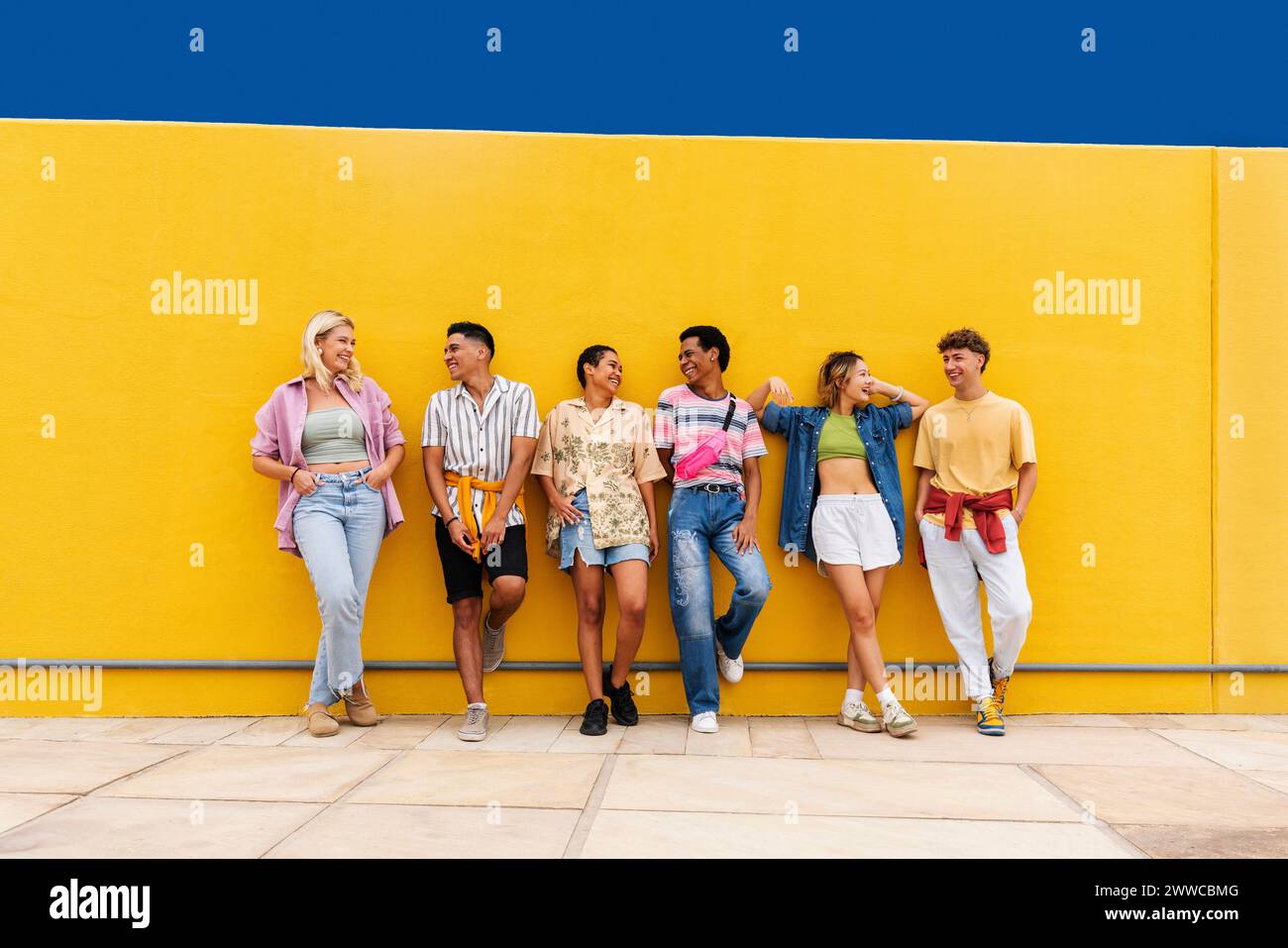 Unbeschwerte Freunde in bunter Kleidung, die vor der gelben Wand plaudern Stockfoto