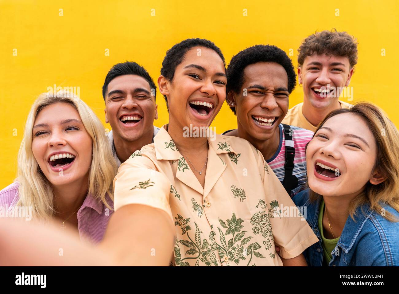 Porträt lachender multiethnischer Freunde an der gelben Wand Stockfoto